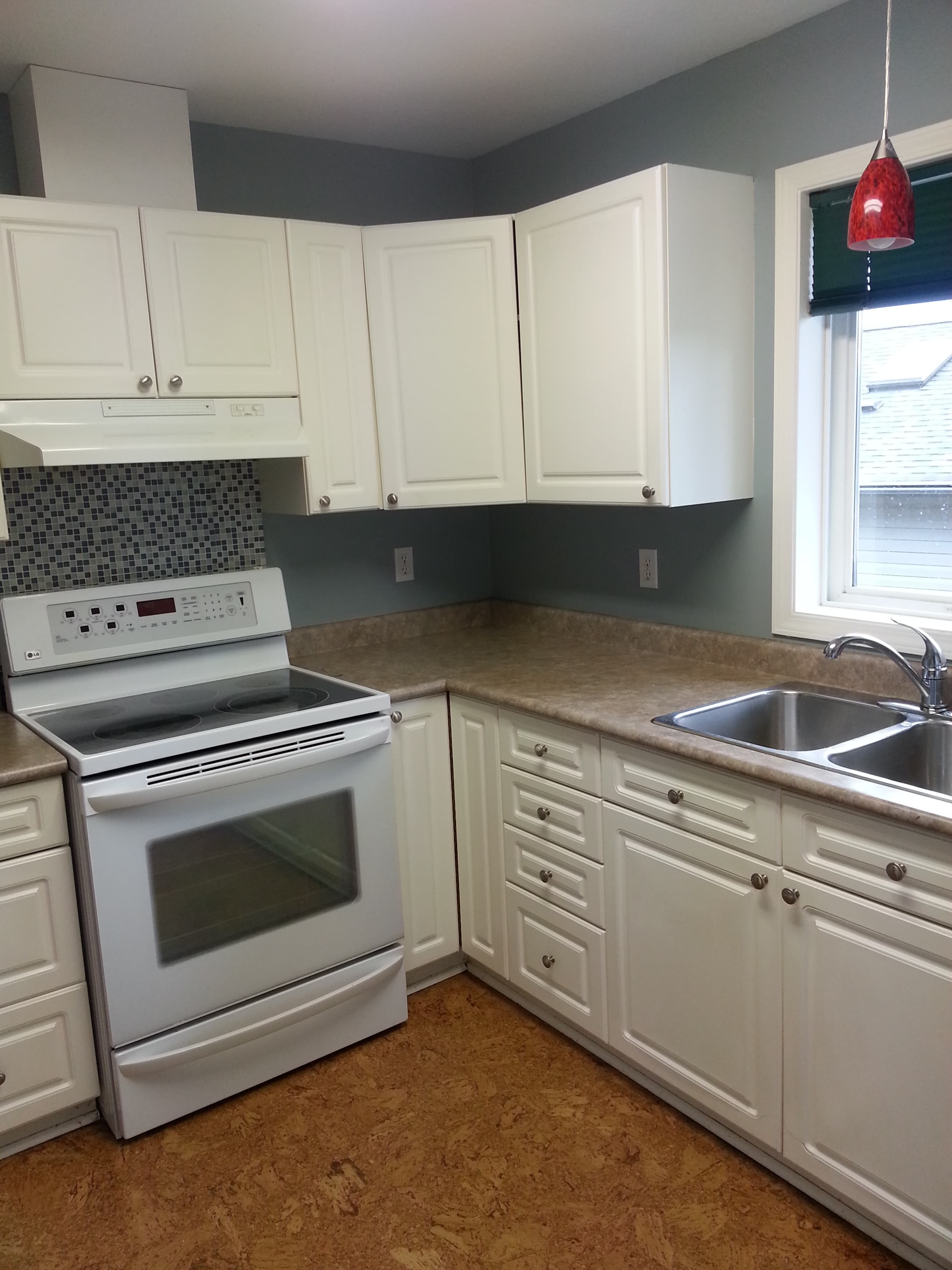 Kitchen before renovation with white cupboards, an electric cooker, mosaic backsplash, and cork flooring